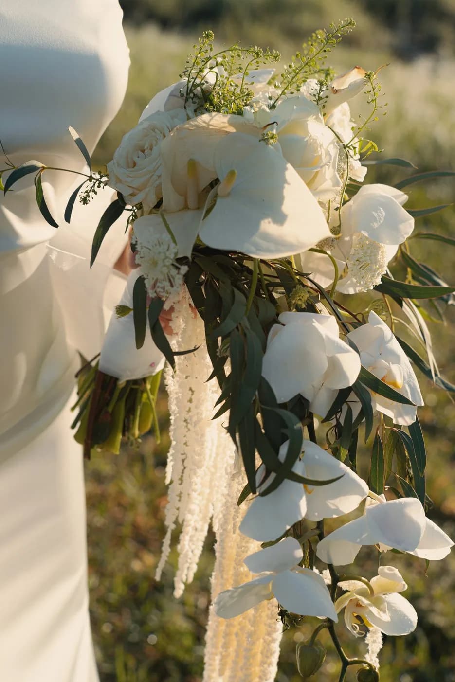 A white bridal bouquet of orchids, roses, and trailing amaranthus