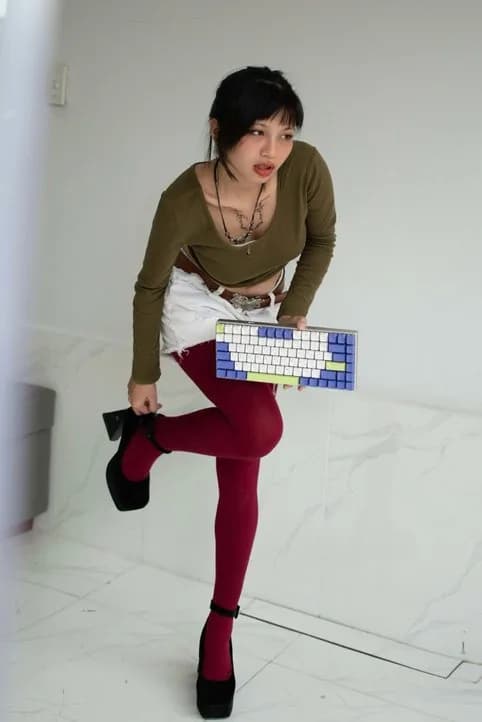 Hoàng Anh holding a custom mechanical keyboard, olive top and red tights
