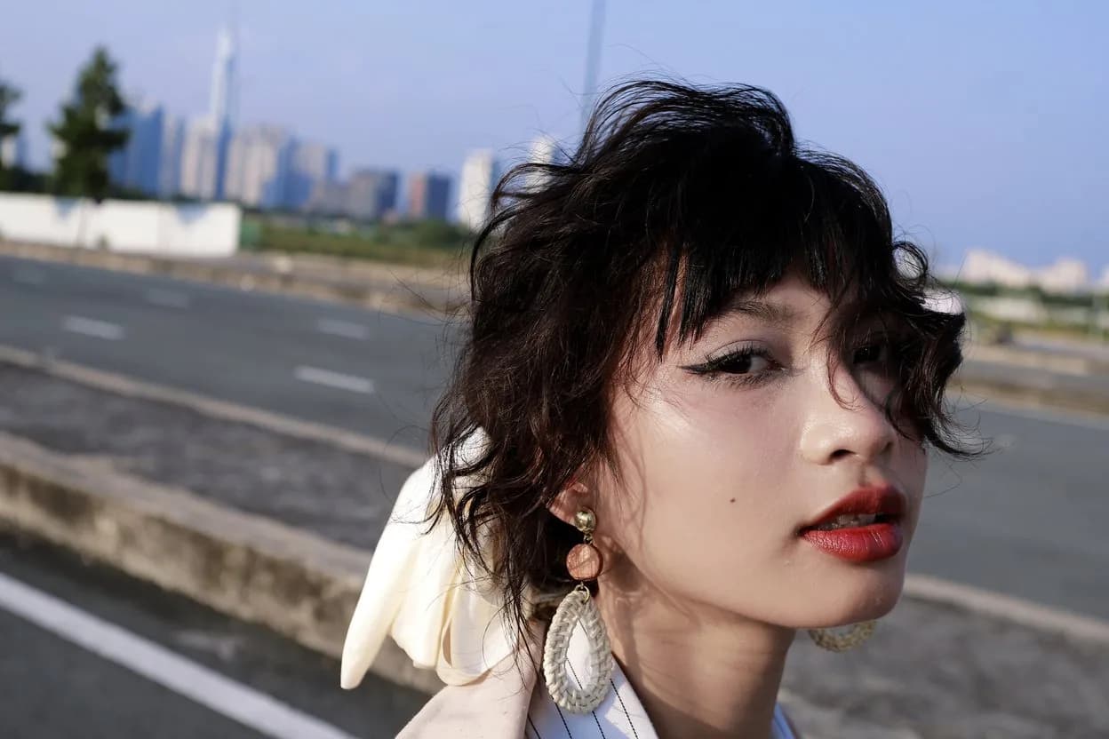 Close portrait of Hoàng Anh with windblown hair beside an empty road and the city