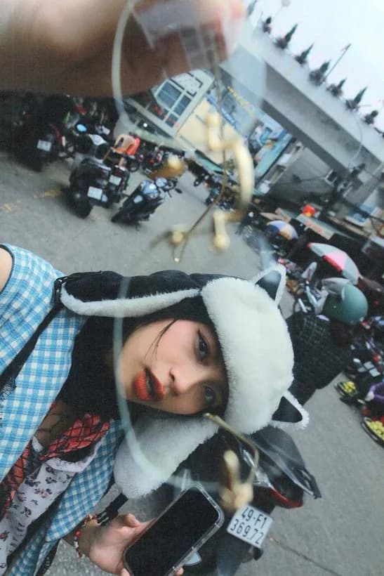 Close portrait of Hoàng Anh in a fuzzy hat on a scooter, city traffic behind her